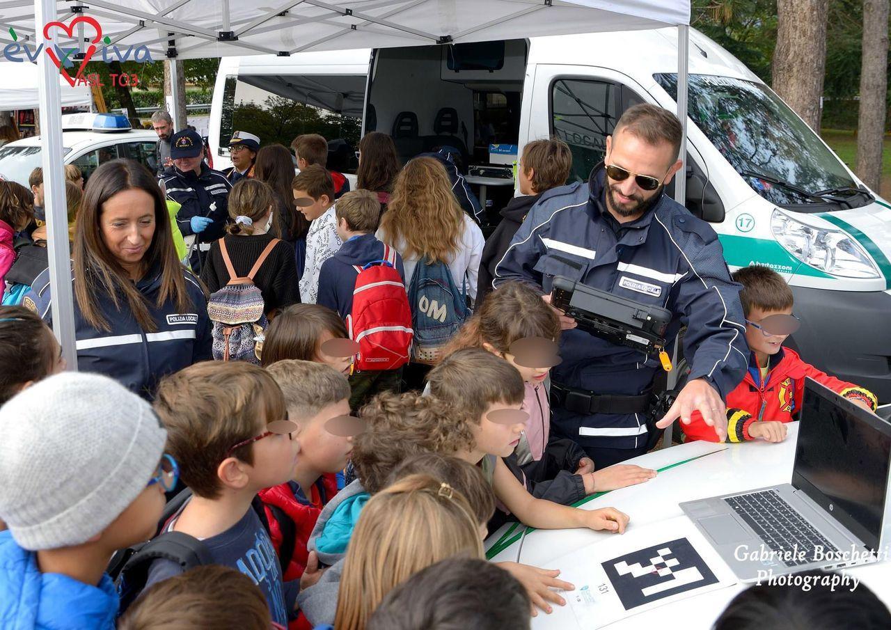 Agente della Polizia Locale che mostra un dispositivo elettronico a un gruppo di bambini delle scuole